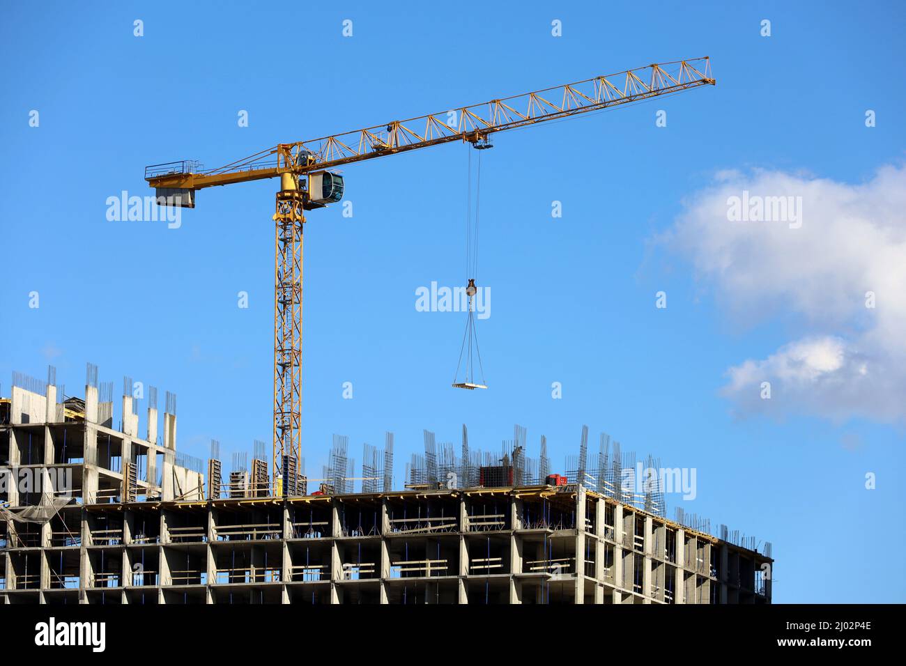 Bau Turmkran mit Ladung über unfertigen Wohngebäude auf blauem Himmel Hintergrund. Wohnungsbau, Arbeiter auf Gerüsten Stockfoto