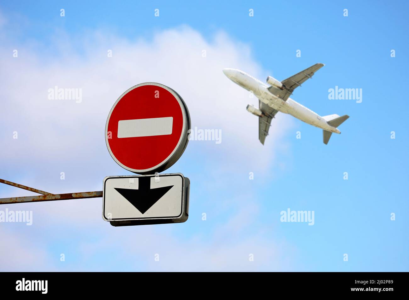 Stoppschild mit Pfeil nach unten und Flugzeug in blauem Himmel. Konzept der Band für Flüge über Europa aus Russland, Sanktionen wegen russischer Operation in der Ukraine Stockfoto