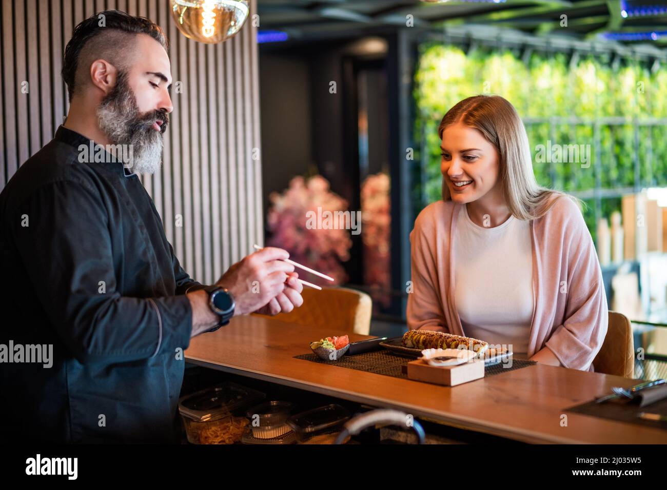 Sushi-Meister lehrt junge Frauen, wie man Essstäbchen im Sushi-Restaurant verwendet. Stockfoto