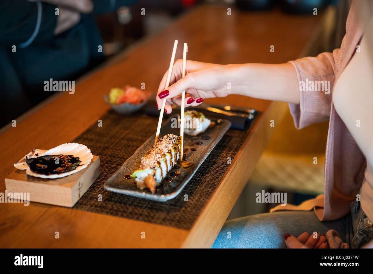 Nahaufnahme einer Frau, die im Sushi-Restaurant Umami-Sushi mit Essstäbchen isst. Stockfoto