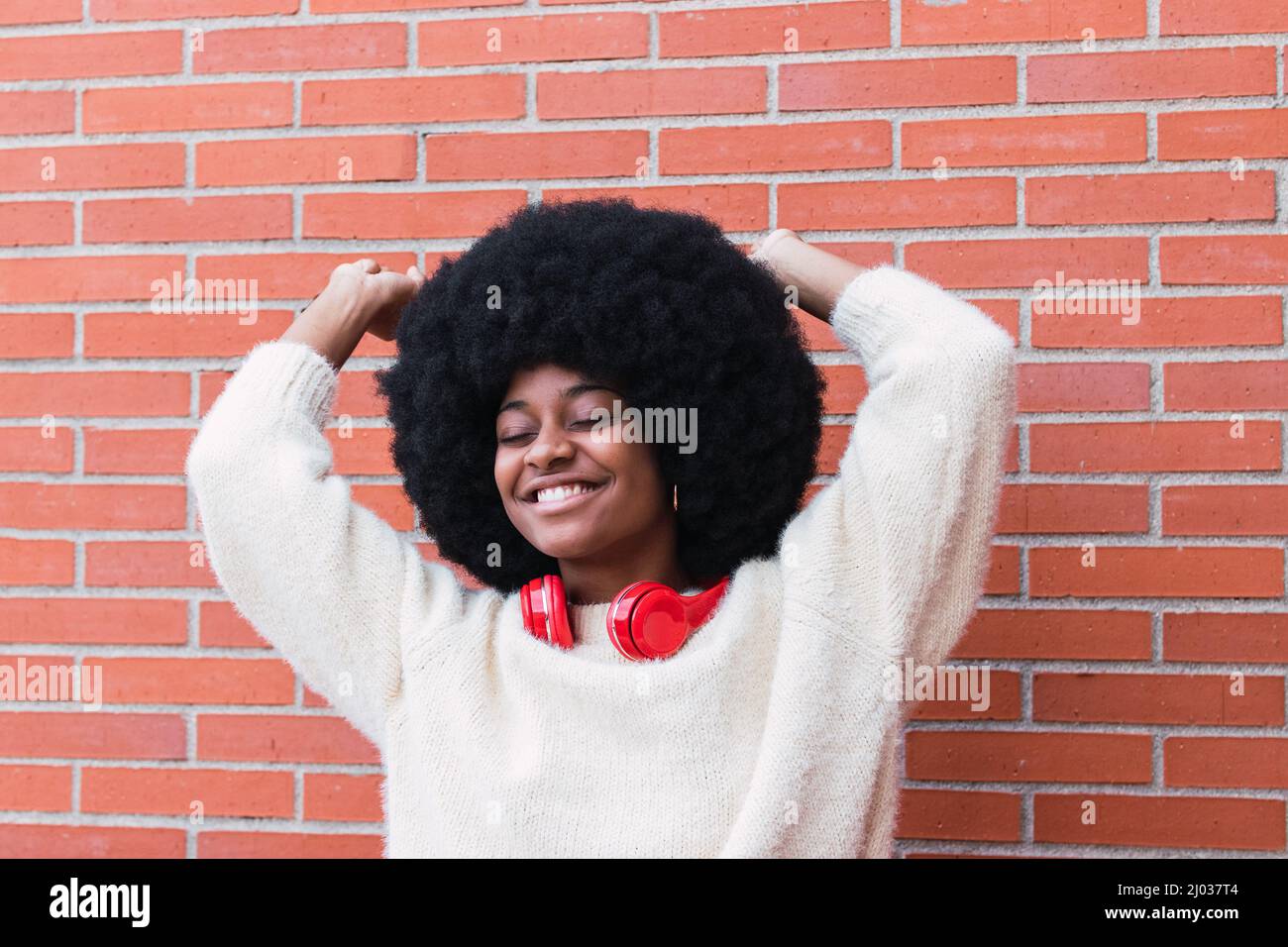 Schöne schwarze Frau mit roten Kopfhörern am Hals, Afro-Frisur und perfekten weißen Lächeln tanzen, Spaß haben und lächeln mit geschlossenen Augen. Speicherplatz kopieren Stockfoto