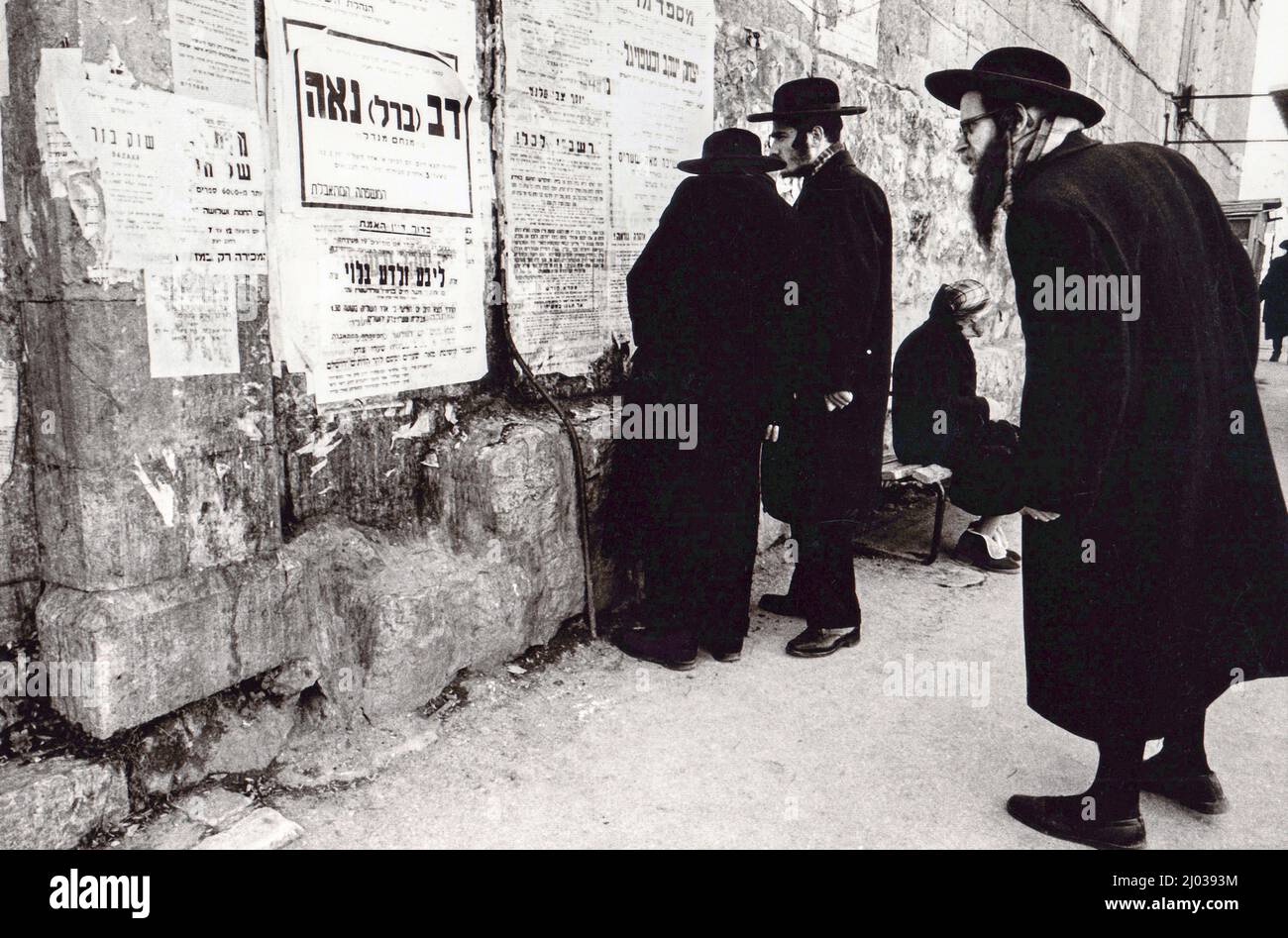 Ultraorthodoxe jüdische Männer lesen um 1975 Zeichen auf Hebräisch und Jiddisch an einer Wand in der Mea Shearim-Abteilung von Jerusalem Stockfoto