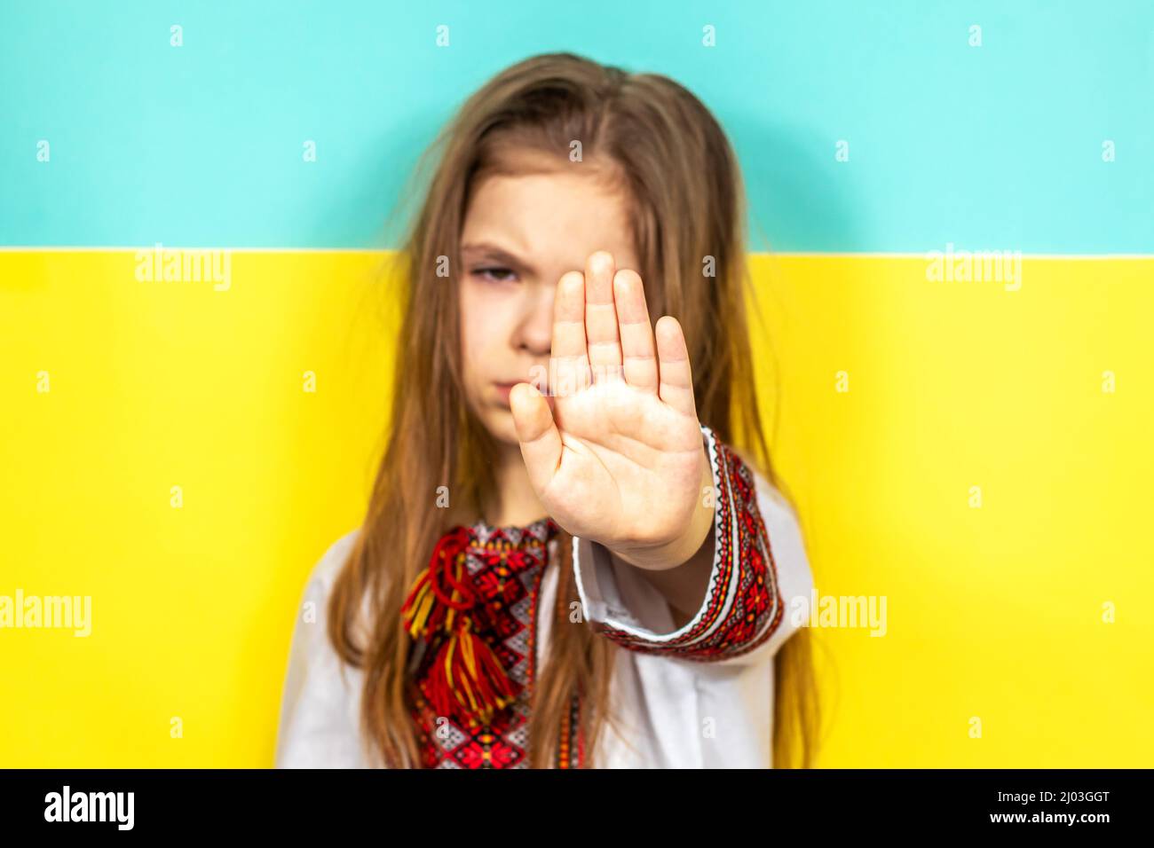 Ein Mädchen in ukrainischer Nationalkleidung, ein besticktes Hemd, streckte ihre Hand vor den Hintergrund der ukrainischen Flagge. Beendet den Krieg in der Ukraine Stockfoto