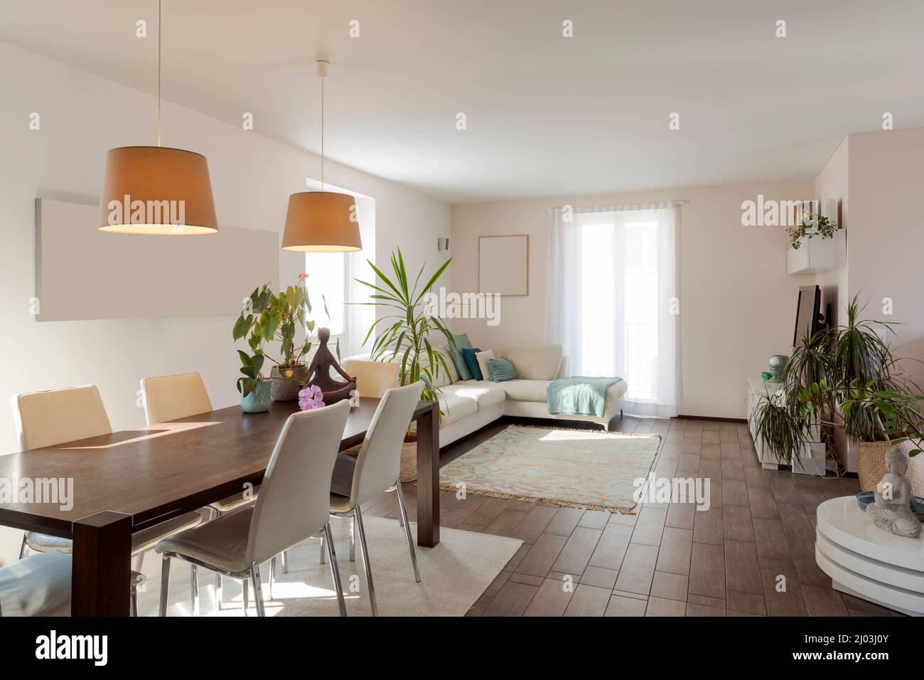 Großes Wohnzimmer mit Esstisch, hellen Stühlen und einem großen Sofa. Große, helle Fenster. Modernes Design-Apartment Stockfoto