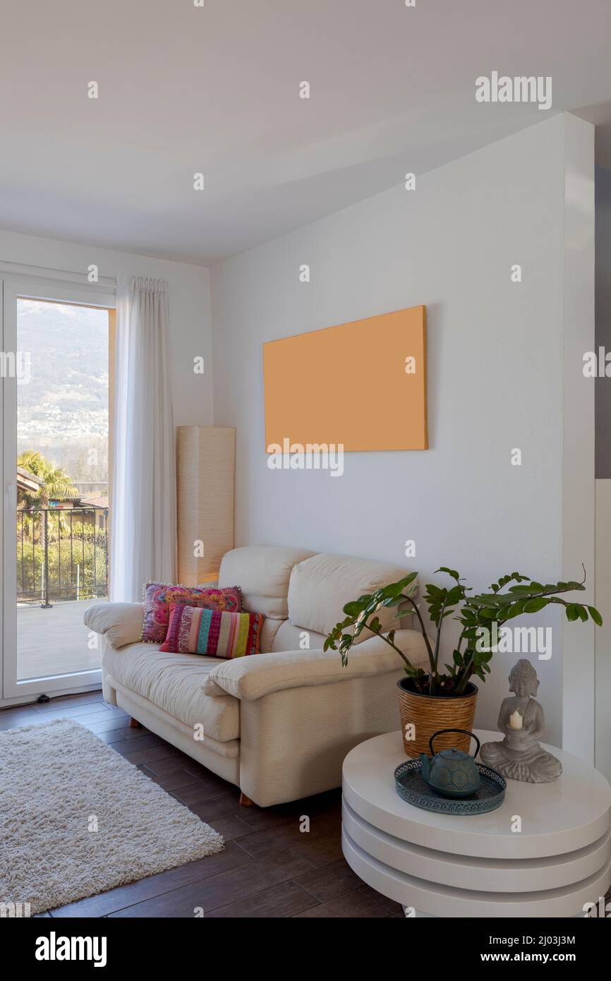 Kleines Wohnzimmer mit Sofa und bunten Kissen. Es gibt einen kleinen Tisch mit einer Pflanze darauf. Fenster mit Blick auf die Natur. Niemand drinnen Stockfoto