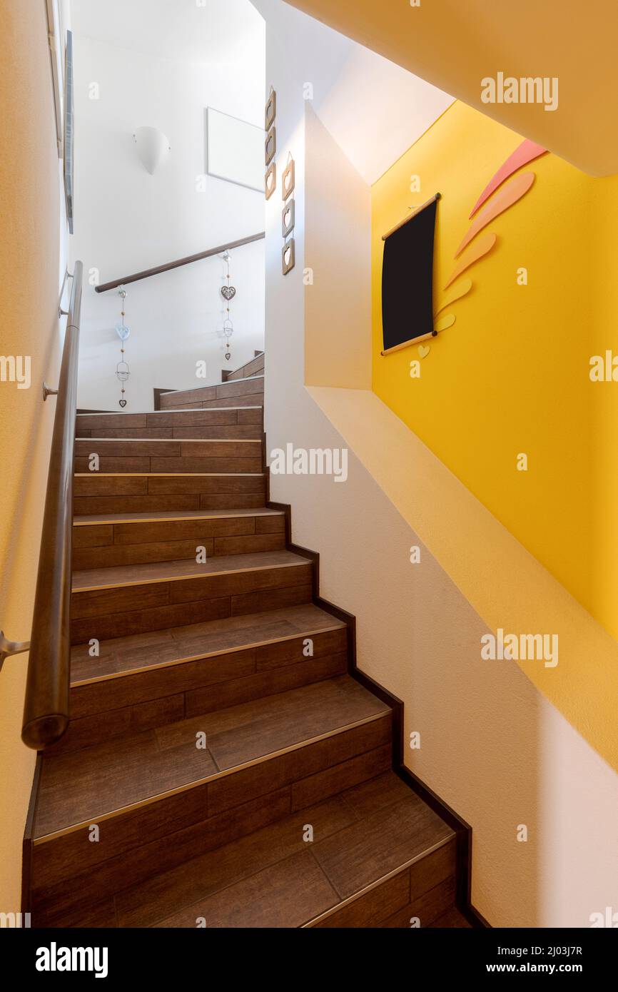 Braune Treppe mit gelben Wänden und hölzernen Handläufen. Niemand drinnen Stockfoto