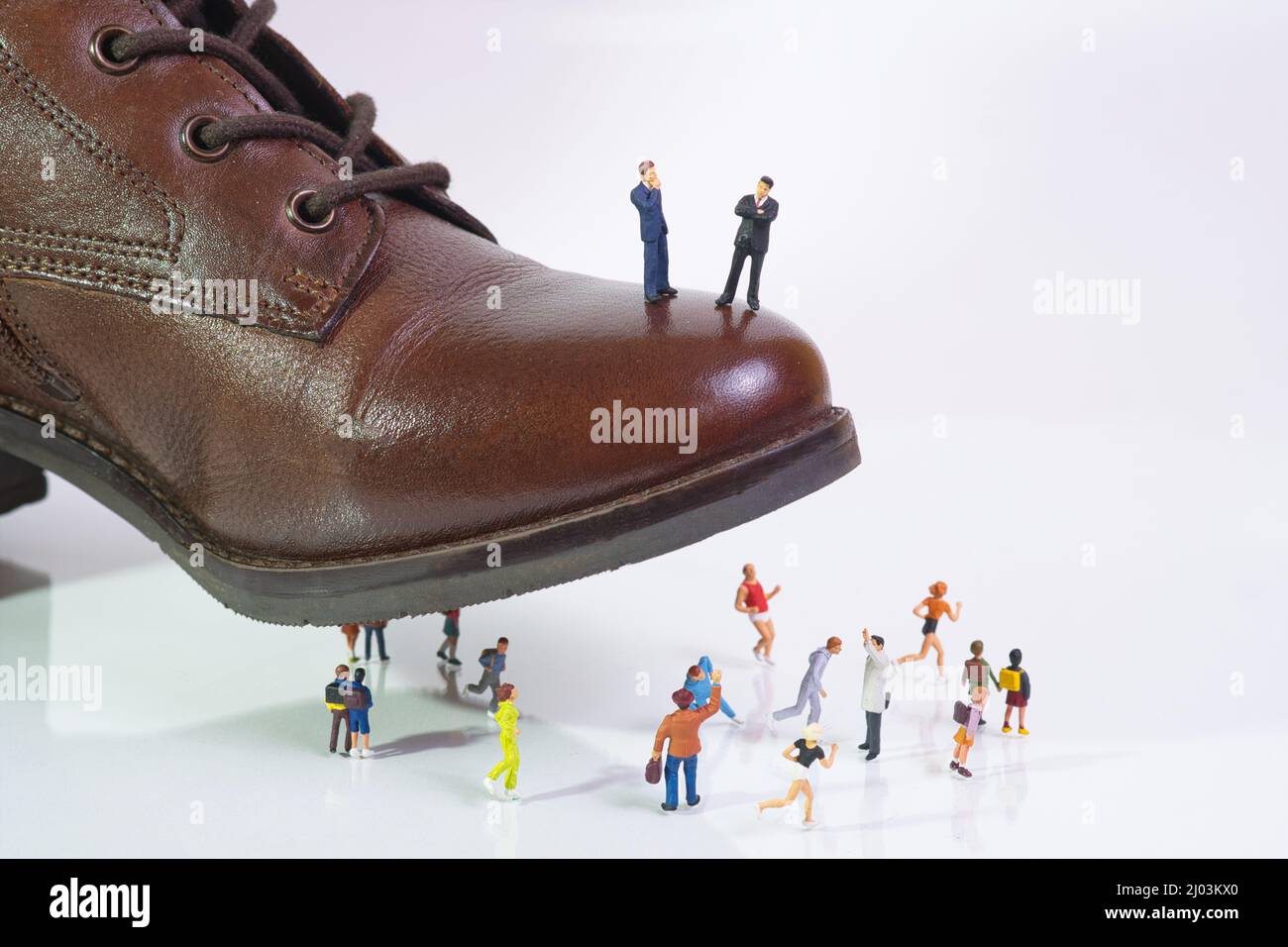Zwei mächtige Geschäftsleute stehen auf einem Schuh, der auf flüchtende Menschen tritt Stockfoto