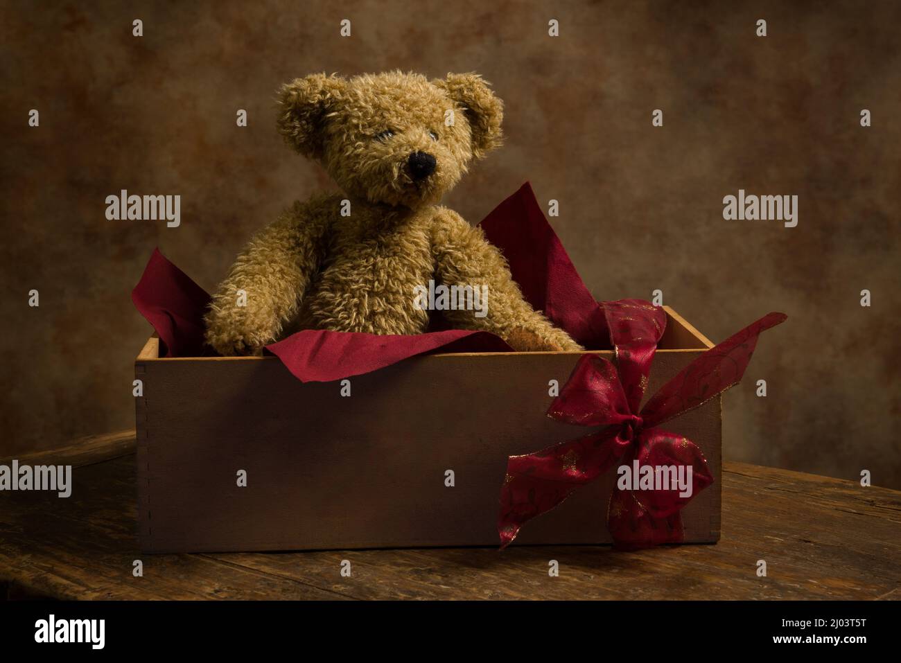 Niedlicher kleiner Teddybär, der in einer Holzkiste mit Geschenkband versteckt ist. Stockfoto