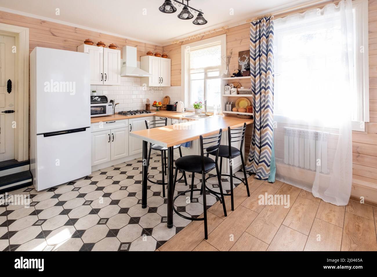 Moderne, weiße U-förmige Küche im skandinavischen Stil. In einem hellen rustikalen Haus, wo die Küche mit dem Wohnzimmer kombiniert wird Stockfoto