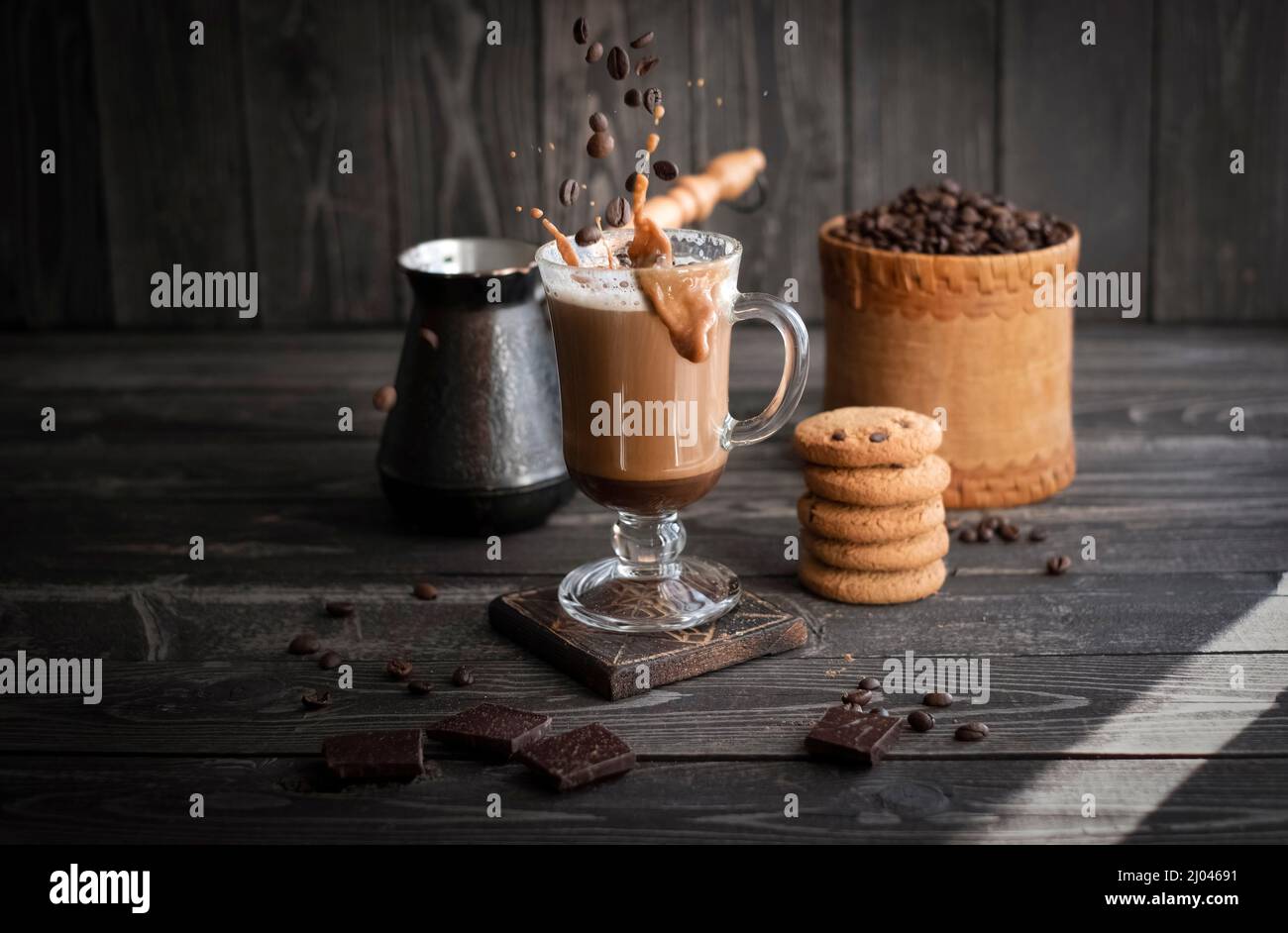 Kaffee mit Creme mit Spritzern und Körnern im Flug mit Keksen auf dunklem Holzhintergrund Stockfoto