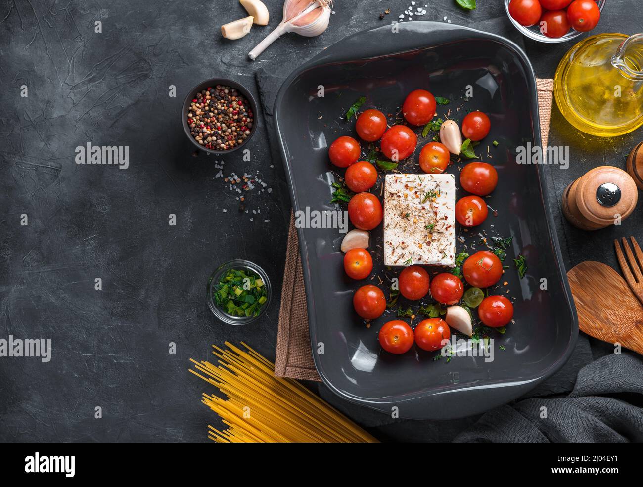 Feta, Kirschtomaten, Gewürze und Spaghetti auf schwarzem Hintergrund. Zutaten für die Herstellung von Feta Paste. Stockfoto
