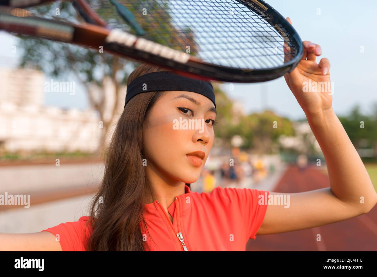 Asiatische junge Frau mit schwarzem Stirnband, die auf dem Tennisplatz steht und einen Tennisschläger hält. Hochwertige Fotos Stockfoto