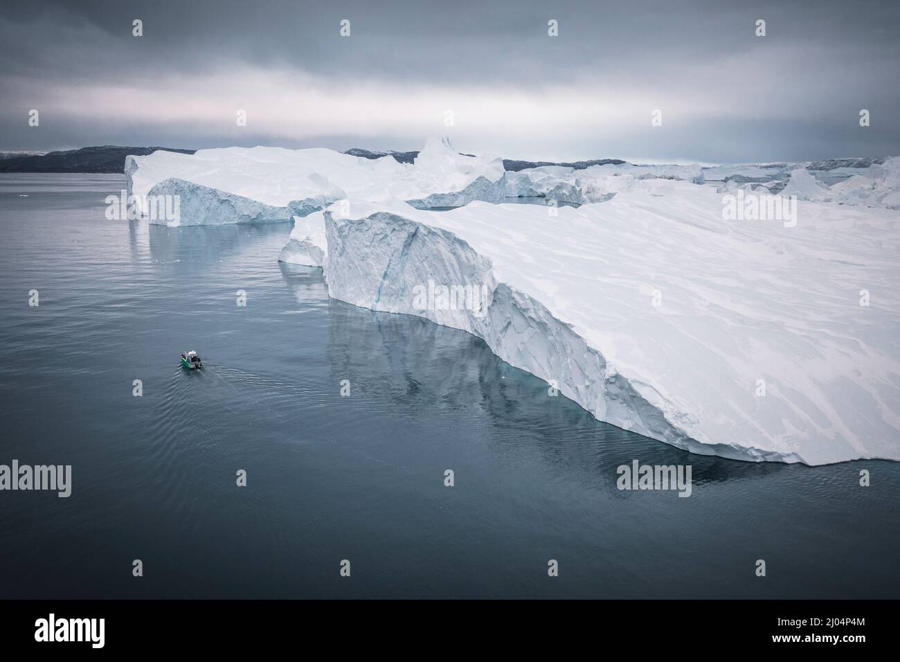 Kleines Boot, das aus der Luft vor extremen Eisbergen segelt Stockfoto