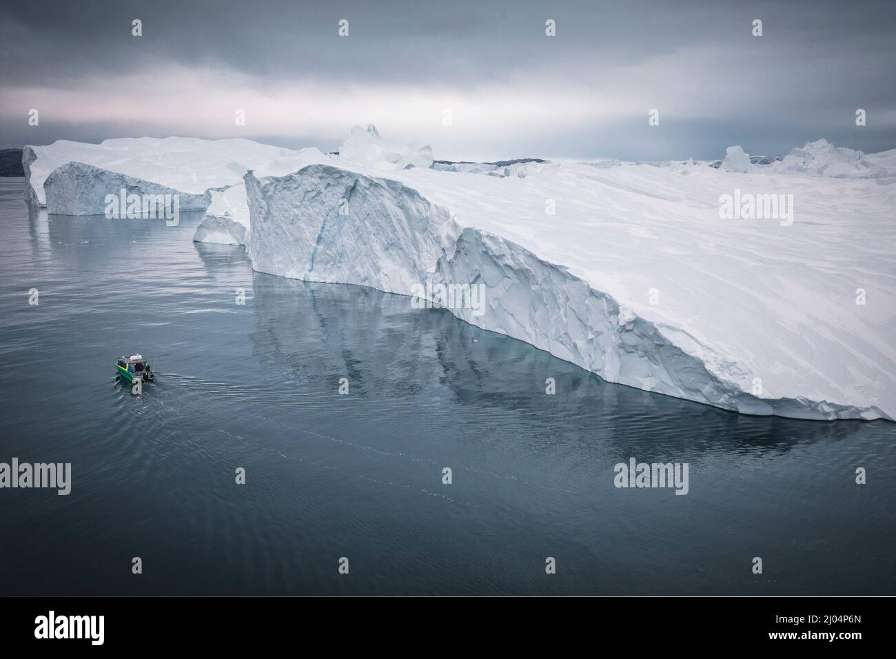 Kleines Boot, das aus der Luft vor extremen Eisbergen segelt Stockfoto