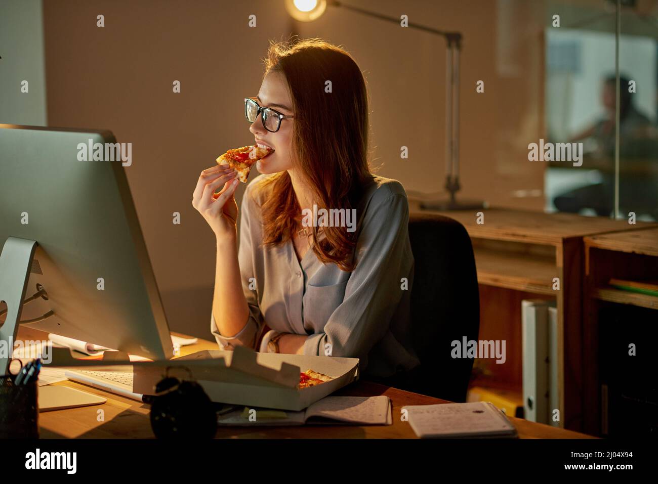 Abendessen spät in der Nacht im Büro. Aufnahme einer attraktiven jungen Geschäftsfrau, die Pizza isst, während sie spät im Büro arbeitet. Stockfoto