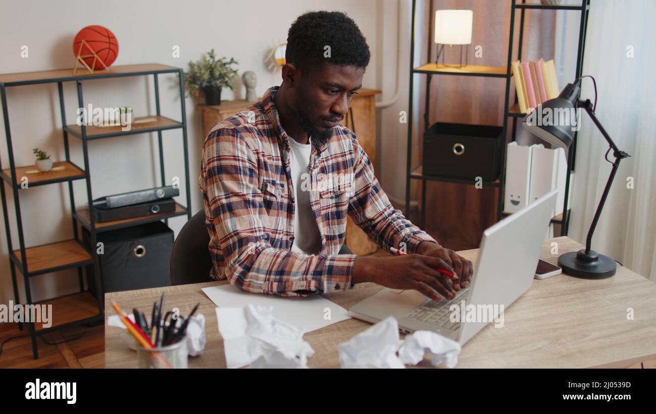 Müder Mann im Heimbüro schlief auf dem Tisch mit Laptop-Computer ein, zerknitterte Blätter Papier Stockfoto