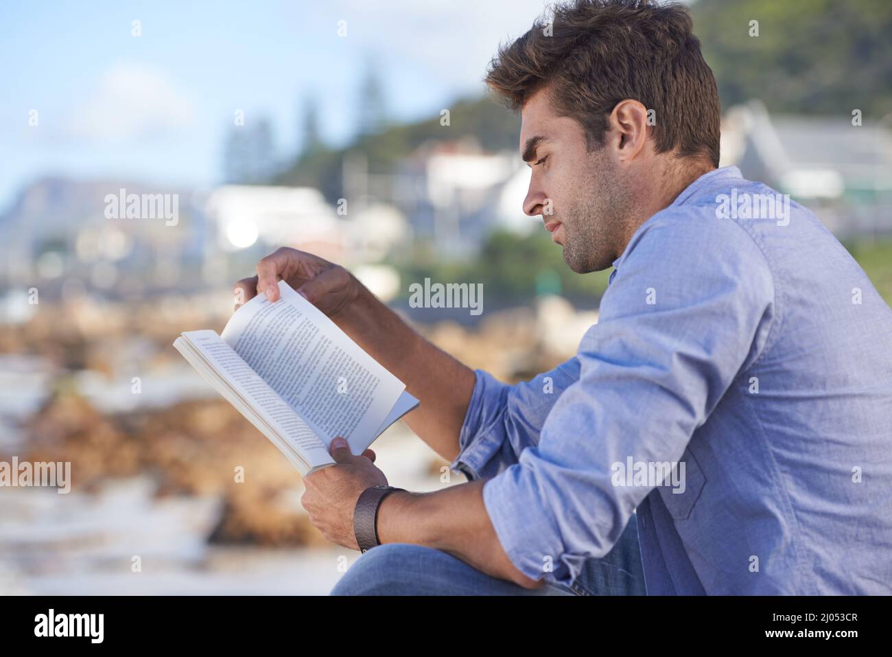 Romane sind eine großartige Möglichkeit, sich zu entspannen. Ein junger Mann, der im Freien ein Buch liest. Stockfoto