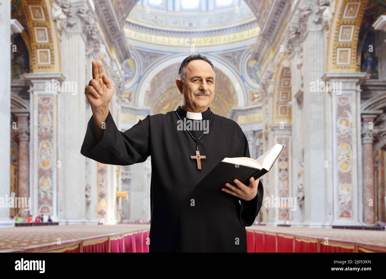 Reifer männlicher Priester, der eine bibel hält und mit der Hand in einer katholischen Kirche gestikuliert Stockfoto