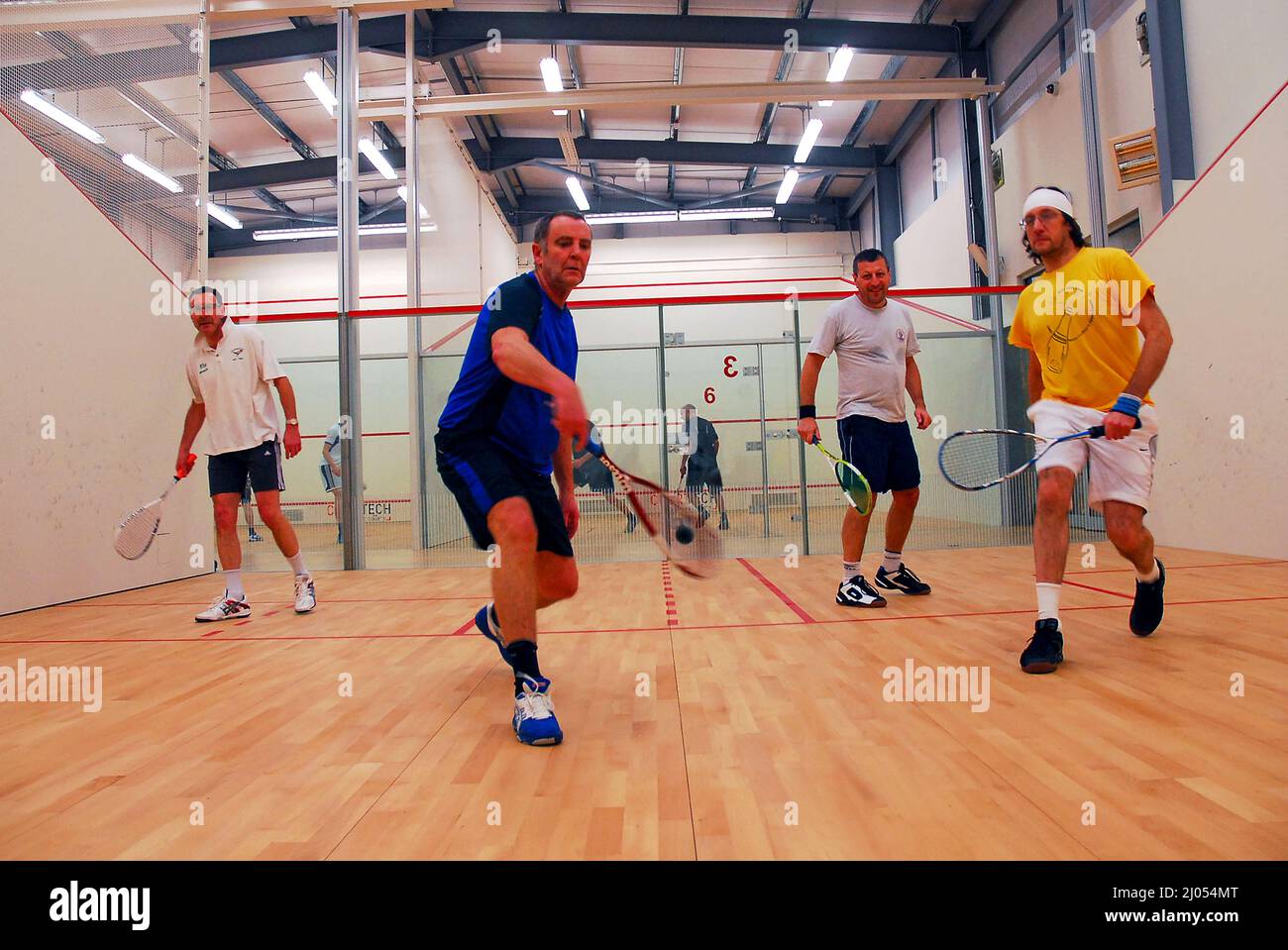 Vier Männer spielen Doppel auf einem speziellen Doppel-Squashplatz. Es gibt zwei Teams spielen ein Spiel, das schnell und ein wenig gefährlich ist. Die meisten Squashplätze sind Einzelplätze, und es ist selten, einen Doppelplatz zu finden. Die Spieler sind im Coolhurst Squash Club in Crouch End, Nord-London, England. Stockfoto
