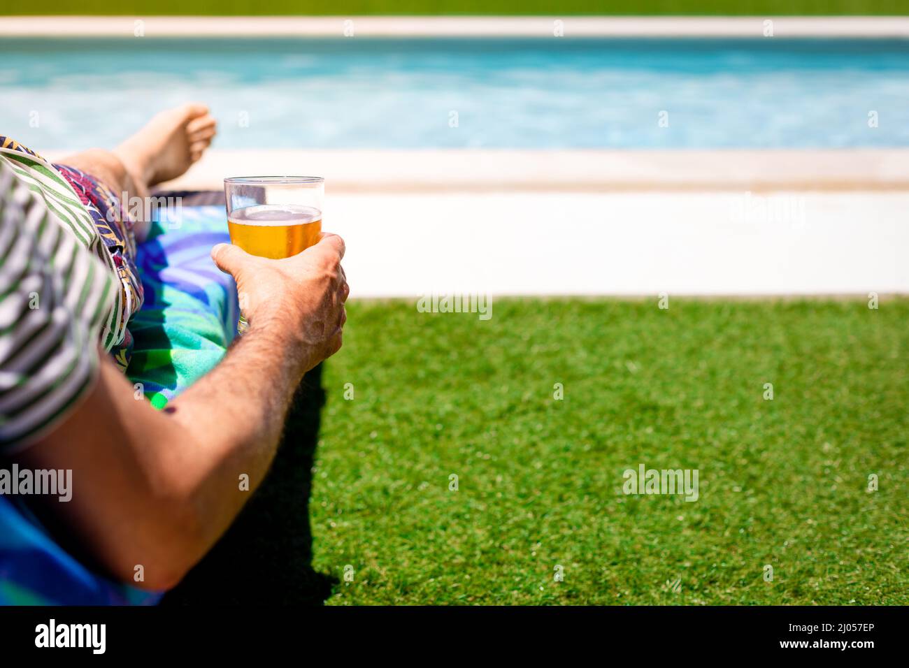 Mittlerer Teil eines Mannes, der sich mit einem Bier in der Hand auf einer Sonnenliege am Pool entspannt. Speicherplatz kopieren Stockfoto