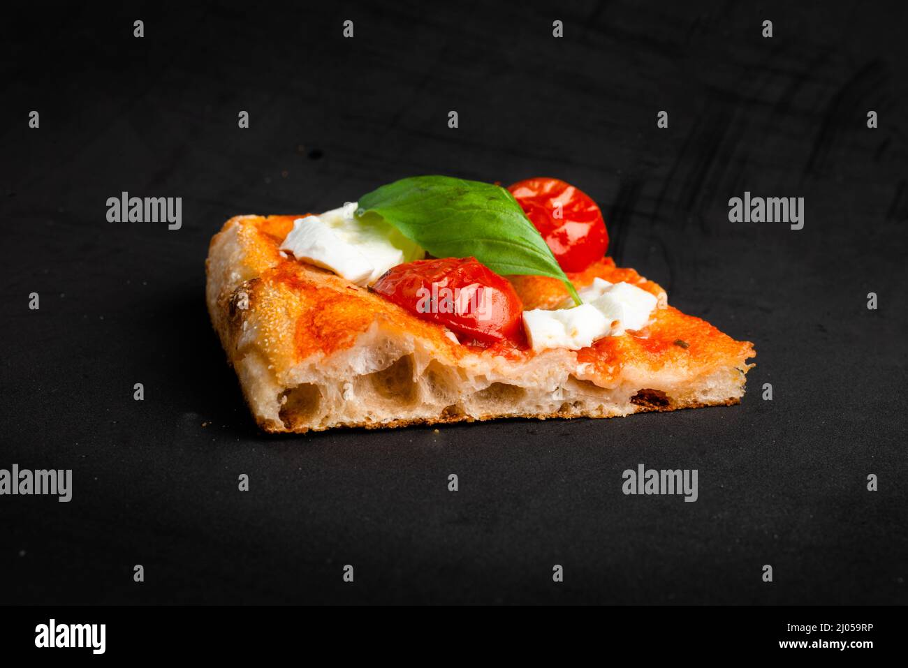 Ein Stück Pizza al Taglio mit Tomaten und Mozzarella isoliert auf schwarzem Hintergrund Stockfoto