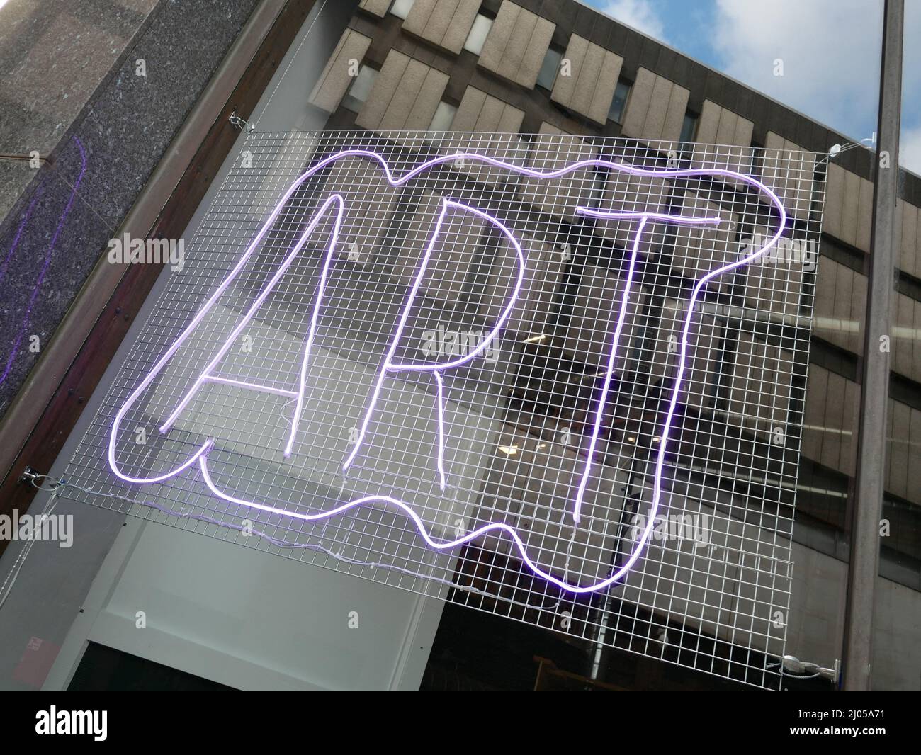 Neon-Kunstschild in einem Fenster mit Spiegelung der umliegenden Straßenlandschaft. Stockfoto