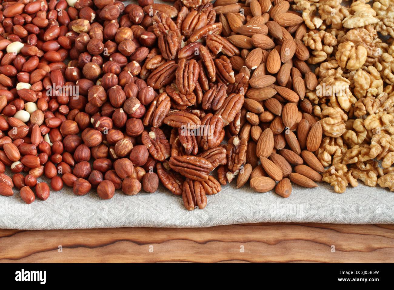 Rohe geschälte Erdnüsse, Haselnüsse, Pekannüsse, Mandeln und Walnüsse auf einem Leinentuch. Nahaufnahme. Makro. Stockfoto