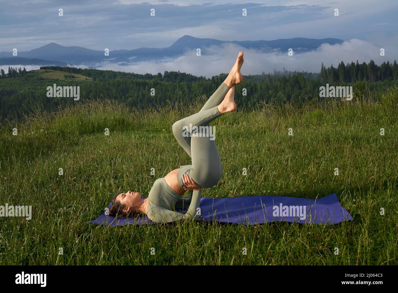 Junge aktive Frau in Sportkleidung, die Fitnessübungen in einer Yogamatte mit herrlichem Blick auf die Berge macht. Konzept der Menschen und gesunde Lebensstile. Stockfoto