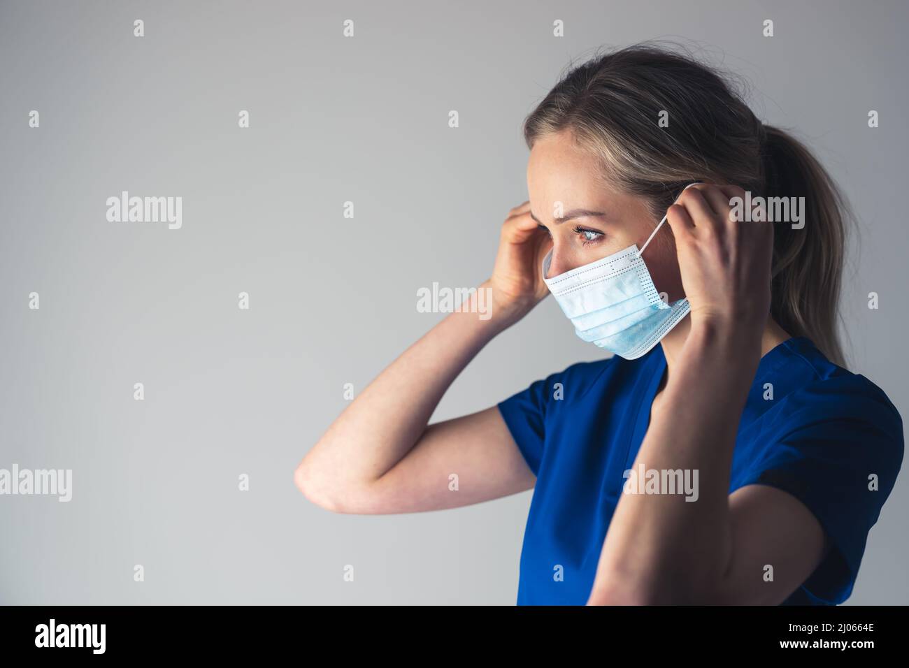 Kaukasische Krankenschwester in blauer Uniform, die eine schützende Gesichtsmaske aufsetzt. Der richtige Weg, um eine Gesichtsmaske auf. Hochwertige Fotos Stockfoto