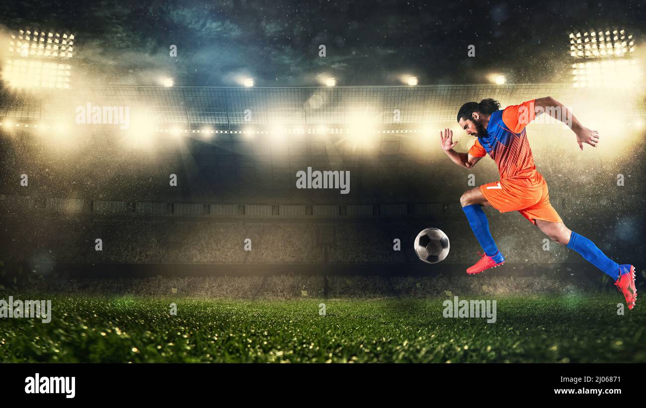 Fußballspieler in orange und blauer Uniform sprintet schnell mit dem Ball im Stadion Stockfoto