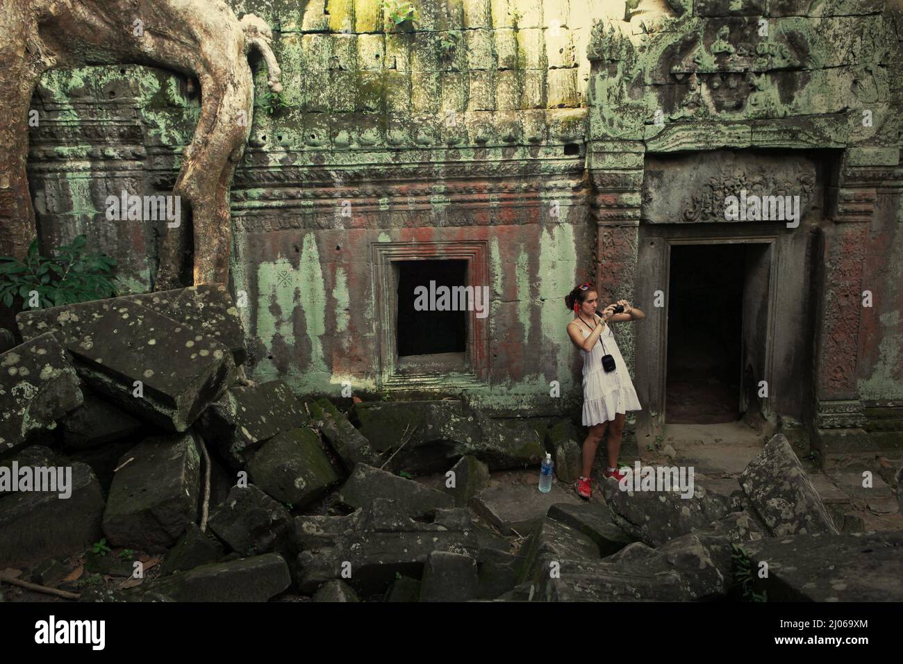 Eine Besucherin, die mit ihrer Handykamera zwischen den Ruinen des Ta Prohm Tempels in Siem Reap, Kambodscha, fotografiert. Einst als Drehort für einen Hollywood-Film von 2001 verwendet Lara Croft: Tomb Raider mit Angelina Jolie und vor allem bekannt für seine riesigen Wurzeln aus wilden Bäumen, die tief zwischen den Steinen verwurzelt sind, war Ta Prohm ein Kloster für Studenten des Mahayana-Buddhismus, bevor es verlassen und für Hunderte von Jahren vergessen wurde. Stockfoto