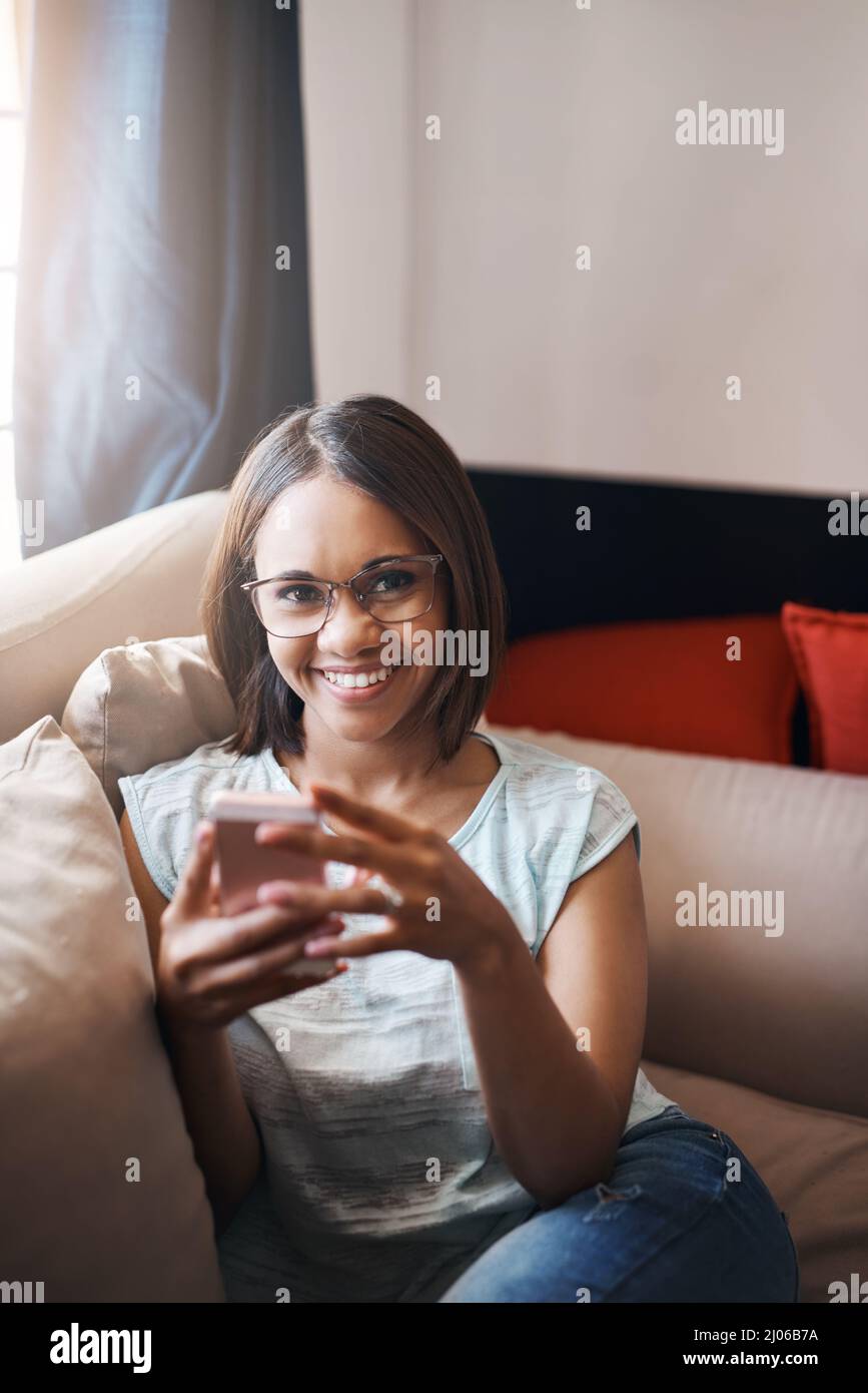 SMS schreiben und entspannen. Ausgeschnittene Aufnahme einer attraktiven jungen Frau, die zu Hause ein Handy benutzt. Stockfoto
