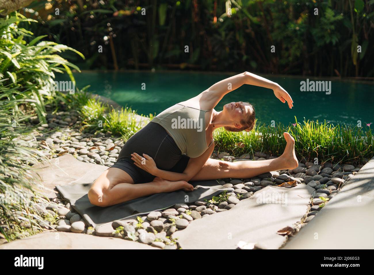 Schwangeren tun Yoga-Posen zu Hause mit Garten auf dem Hintergrund und umarmen ihren Bauch. Sonnenschein, sommerliche Stimmung Stockfoto