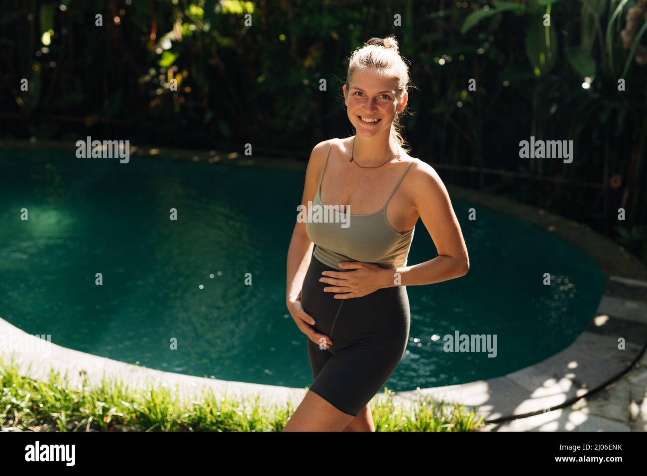 Schwangeren tun Yoga-Posen zu Hause mit Garten auf dem Hintergrund und umarmen ihren Bauch. Sonnenschein, sommerliche Stimmung Stockfoto