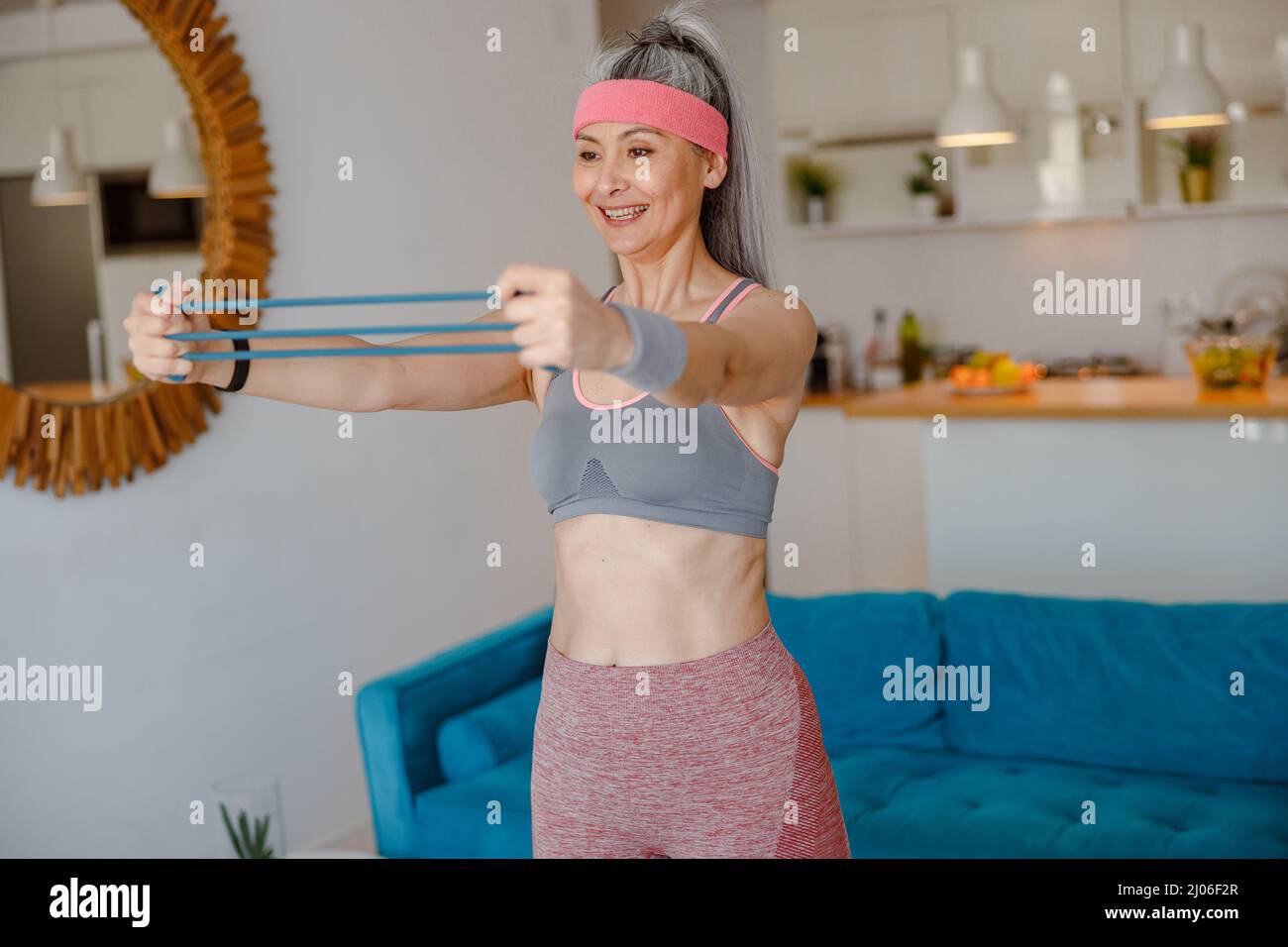Fröhliche Frau mit Armwiderstandsband während des Trainings zu Hause Stockfoto