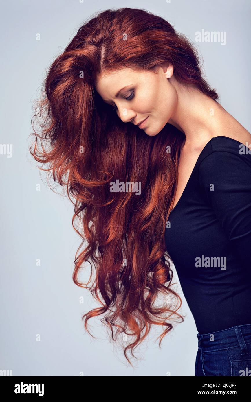 Los, lass deine Haare runter. Studioaufnahme einer jungen Frau mit schönen roten Haaren, die vor einem grauen Hintergrund posiert. Stockfoto