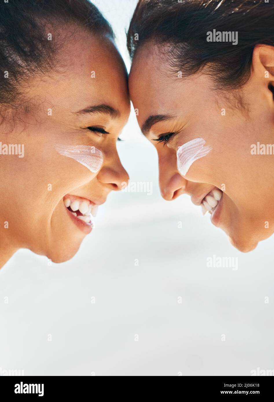 Sonnencreme - Bring die Erinnerungen zurück, nicht die Verbrennung. Aufnahme von zwei schönen jungen Frauen am Strand mit Sonnencreme im Gesicht, die sich gegenseitig anlächeln. Stockfoto