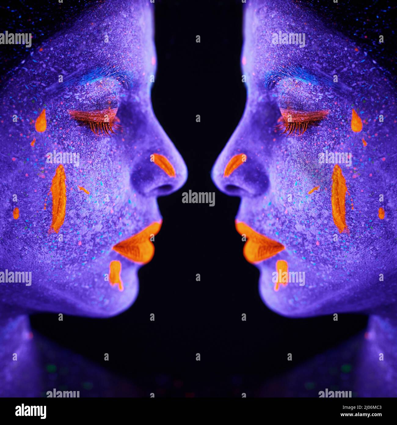 Schwestern in Symmetrie. Spiegelbild einer jungen Frau, die mit Neonfarbe auf ihrem Gesicht posiert. Stockfoto
