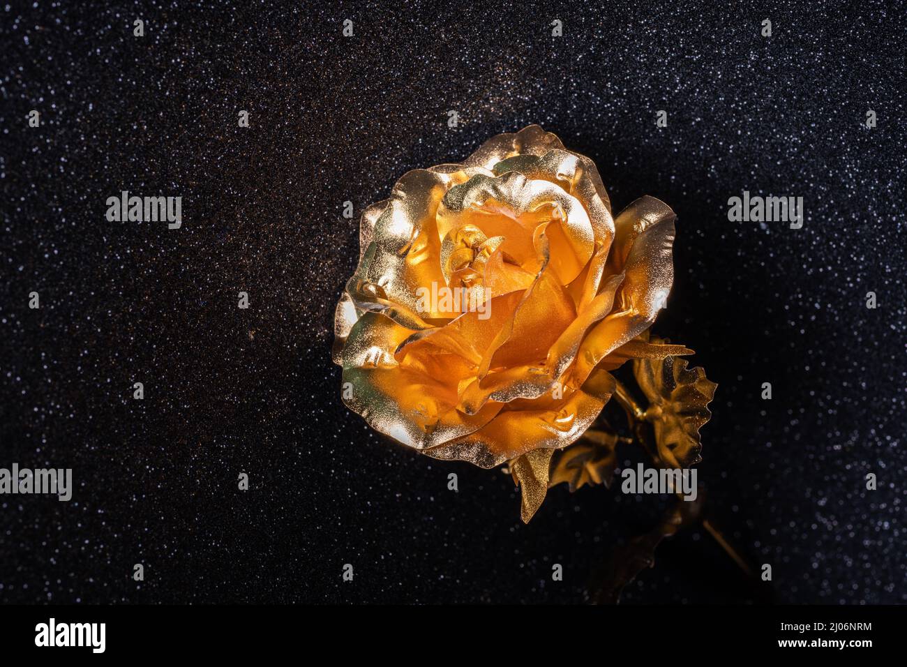 Wunderschöne handgefertigte goldene Rosenblüte aus Metall auf schwarzem Hintergrund mit glänzendem Bokeh, Nahaufnahme. Schmuckgeschenk für einen Urlaub für einen geliebten Menschen. Stilvoller Tren Stockfoto