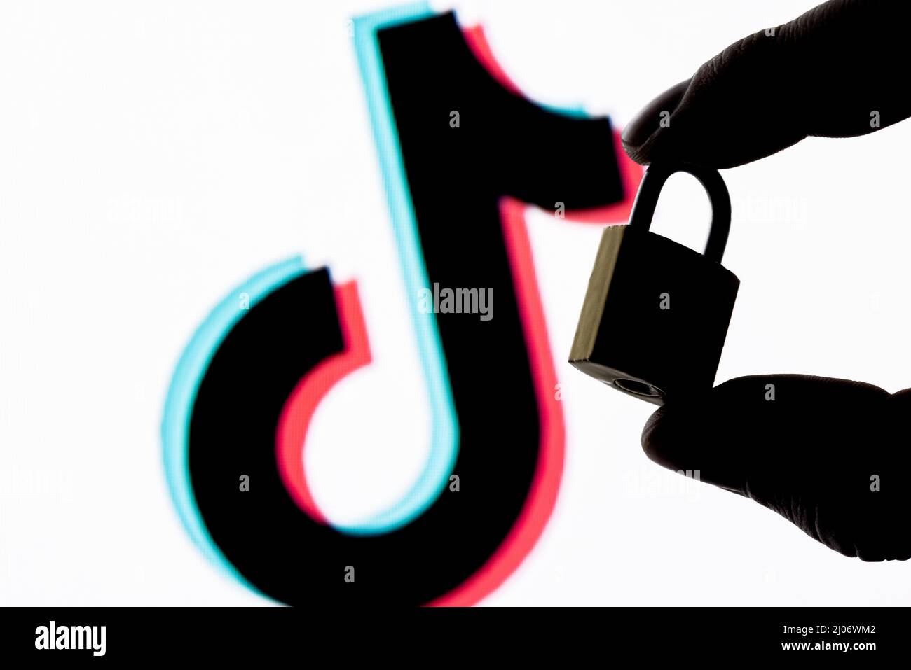 Die Finger halten eine geschlossene Sicherheitsverriegelung auf dem Hintergrund des TikTok Social Network-Logos. Das Konzept der Datensicherheit in TikTok. Stockfoto