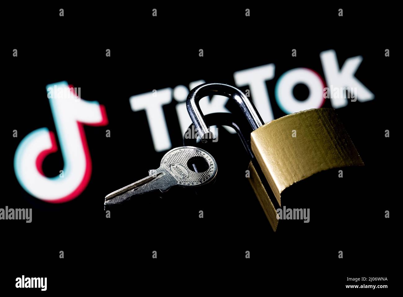 Ein offenes Sicherheitsschloss und Schlüssel auf dem Hintergrund des Logos des sozialen Netzwerks TikTok in der Spiegelreflexion. Stockfoto