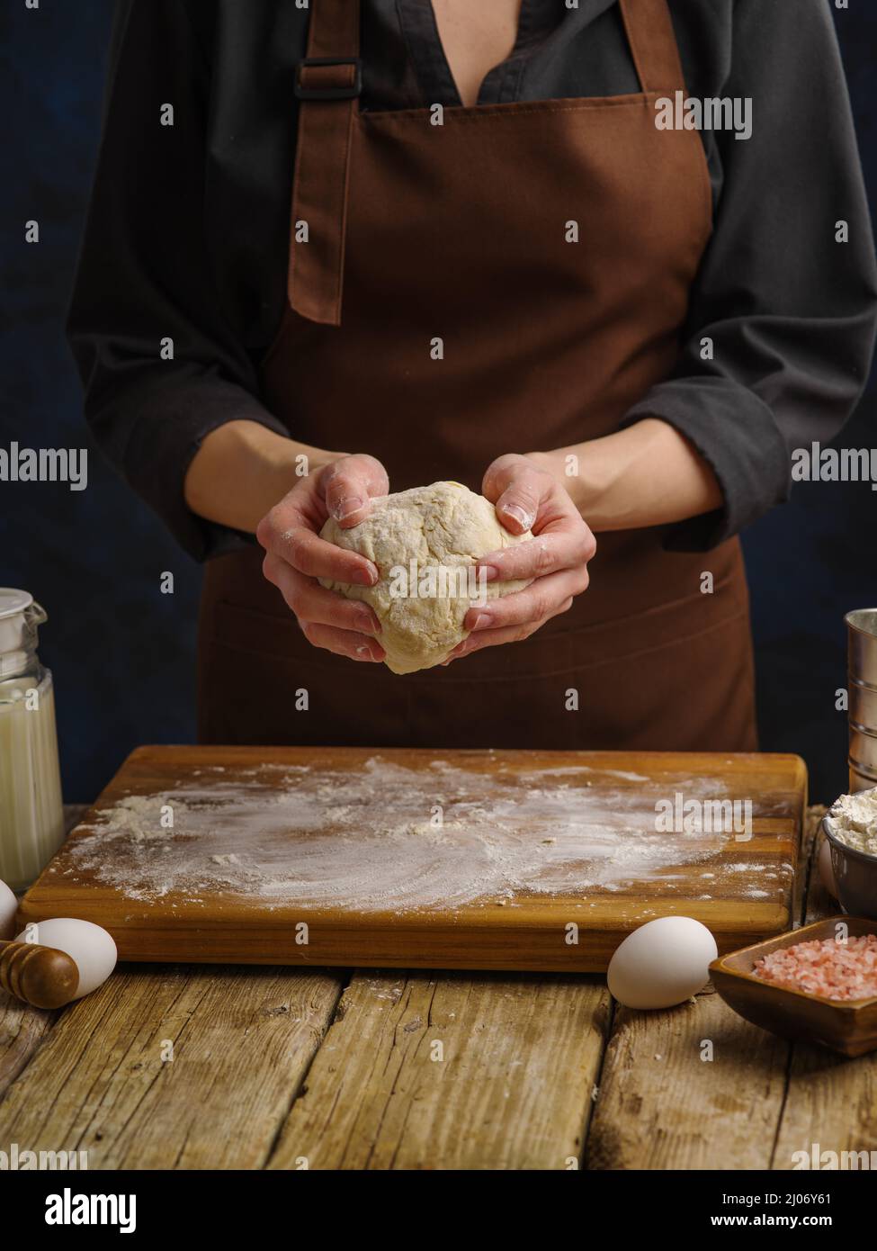 Teig, der von einem professionellen Koch auf einem Holzschneidebrett auf dunklem Hintergrund zubereitet wird. Nahaufnahme. Das Konzept ist Rezepte für die Herstellung von Brot, Pizza, Pasta, Stockfoto