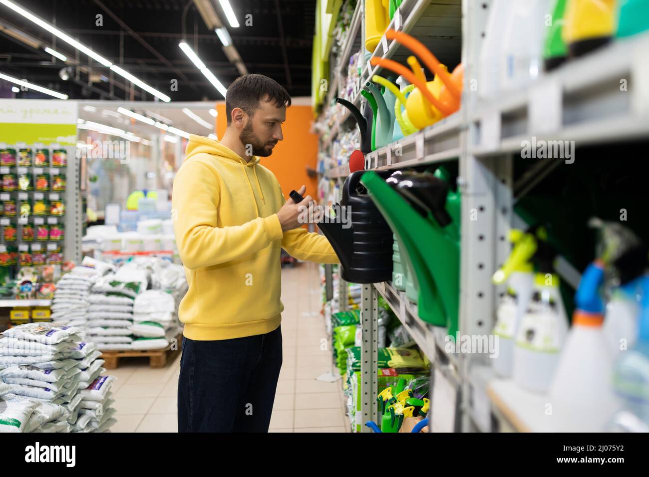 Männlicher Käufer wählt eine neue Gartenbewässerungskannke für die Bewässerung von Pflanzen Stockfoto