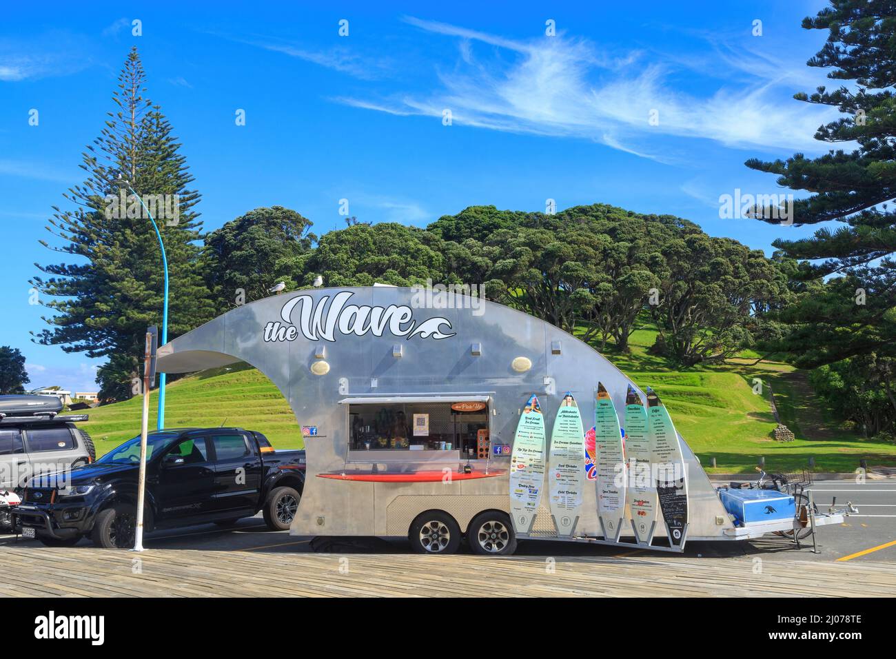 „The Wave“, ein wellenförmiges mobiles Café in Mount Maunganui, Neuseeland. Im Hintergrund ist Mount Drury Stockfoto