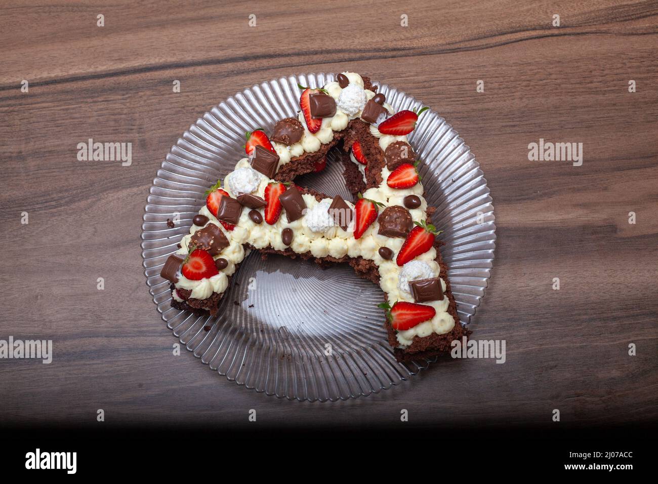 Kuchen in Form des Buchstabens A. Geburtstagskuchen mit Erdbeere und Schokolade. Kuchen mit Schlagsahne und Holzhintergrund. Stockfoto