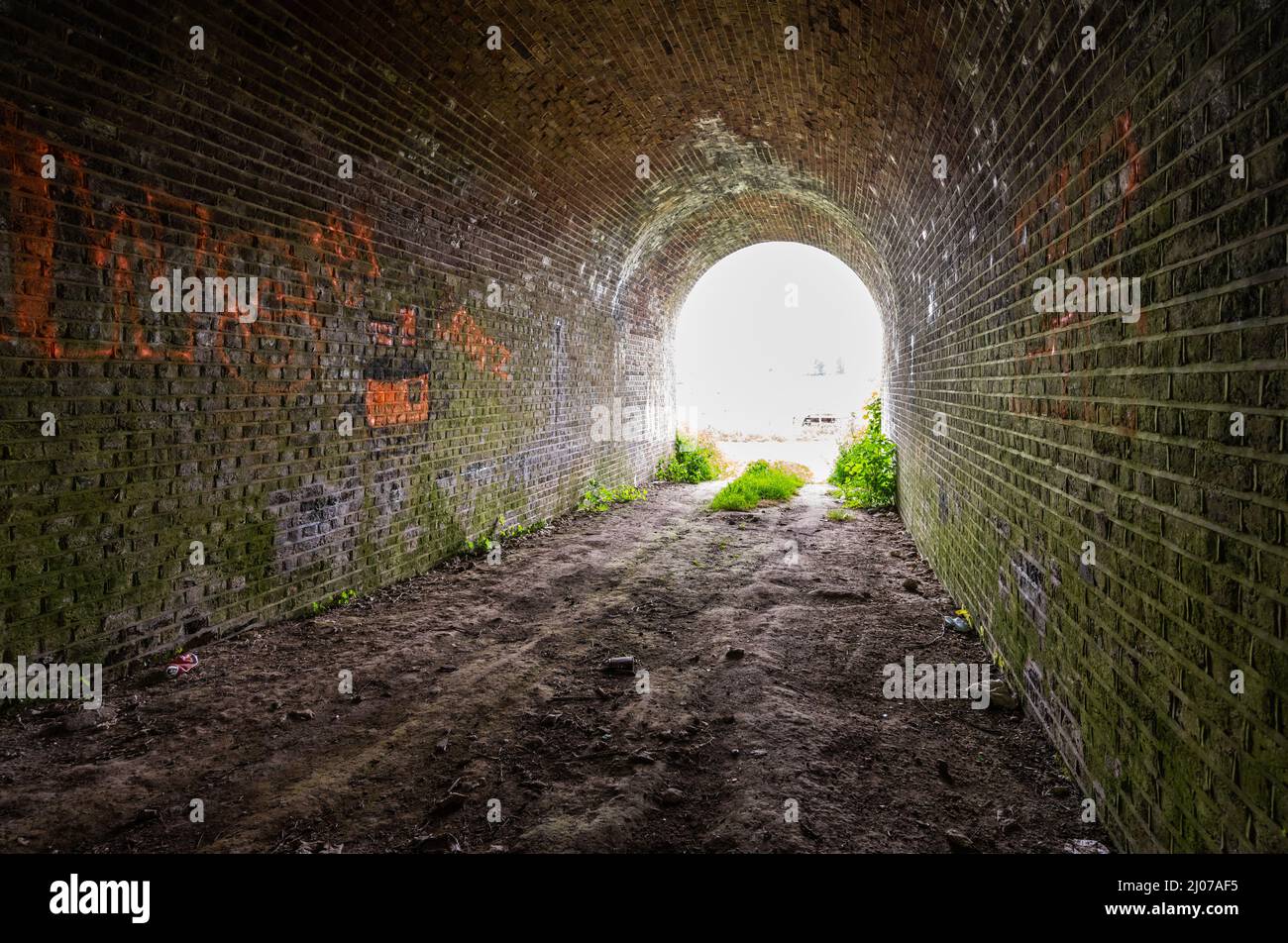 Im Inneren einer Backsteinbrücke unterstreichen sie die Eisenbahnbrücke, scheinbar ein Tunnel, der mit einem Weitwinkelobjektiv in Amberley, West Sussex, England, Großbritannien, auf den Ausgang blickt. Stockfoto