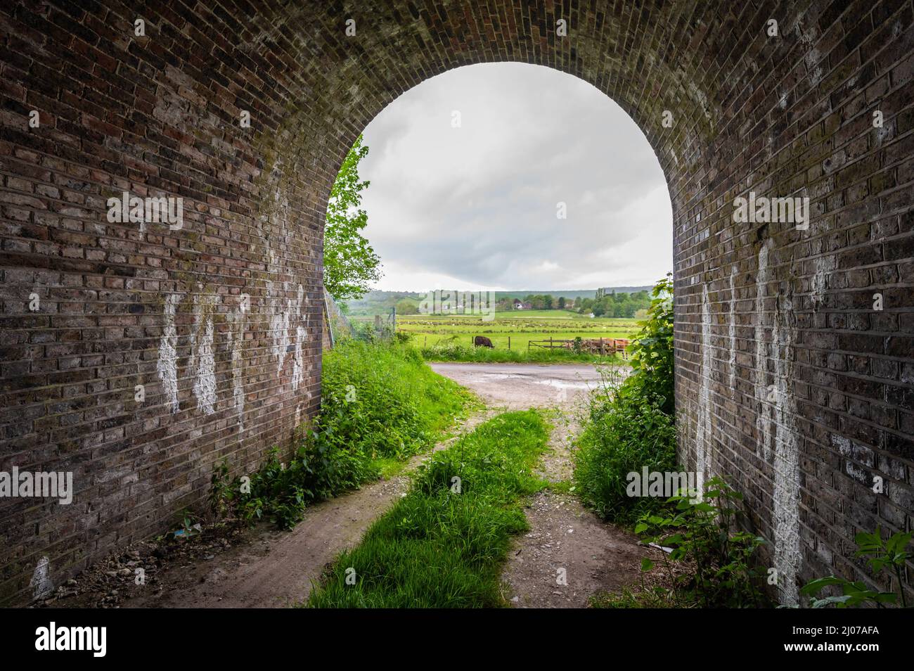 Im Inneren einer Backsteinbrücke unterstreichen sie die Eisenbahnbrücke, scheinbar ein Tunnel, der mit einem Weitwinkelobjektiv in Amberley, West Sussex, England, Großbritannien, auf den Ausgang blickt. Stockfoto