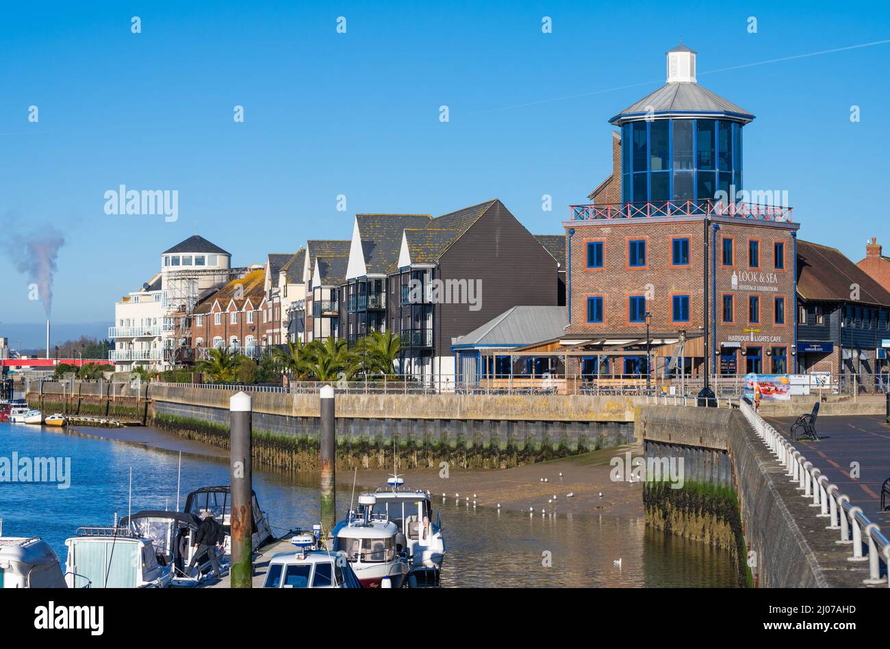 Blick auf die Häuser am Flussufer und das Besucherzentrum von Look & Sea mit Booten, die auf einem Ponton am Fluss Arun in Littlehampton, West Sussex, Großbritannien, festgemacht sind. Stockfoto