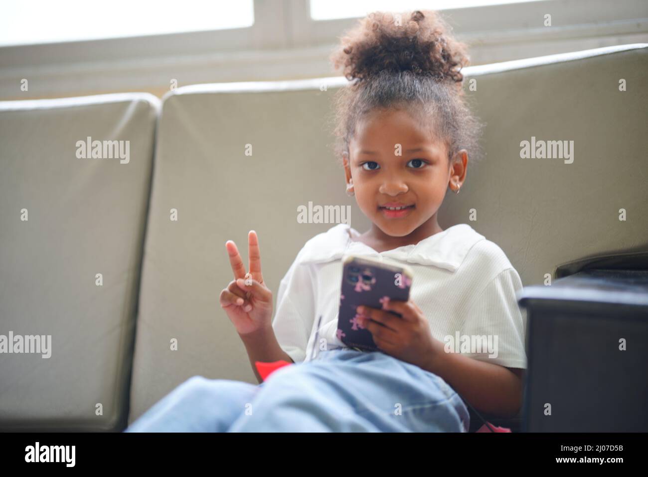 Porträt eines afroamerikanischen Kindes, das auf dem Sofa mit beweglicher Divice sitzt. Stockfoto