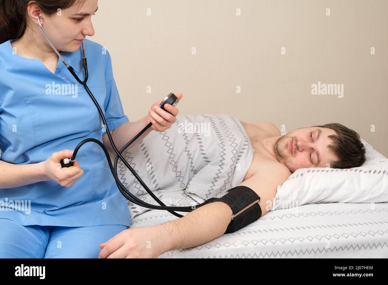 Der Arzt misst den Blutdruck eines jungen 30-jährigen Mannes, der im Bett liegt. Erkrankungen des Herzens und der Blutgefäße beim Menschen, mechanisch Stockfoto